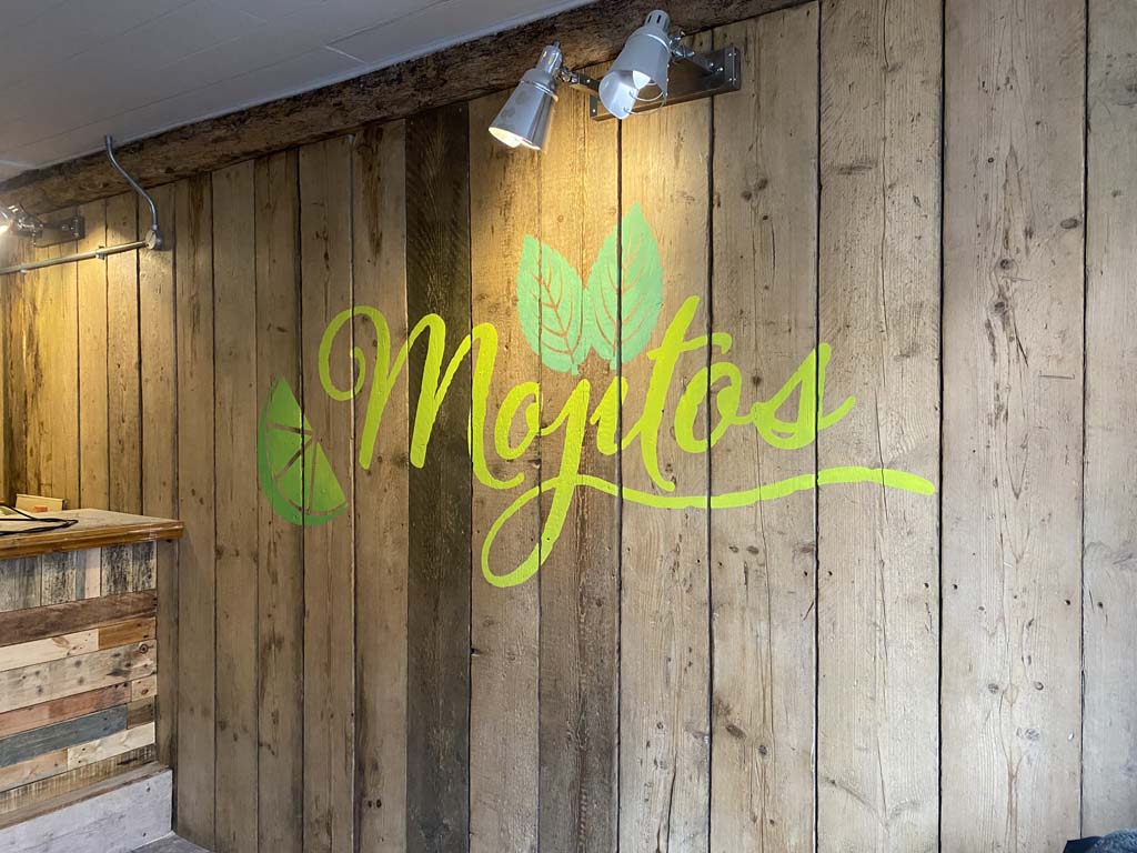 Photo of a wall with a hand painted business logo in bright greens it reads Mojitos