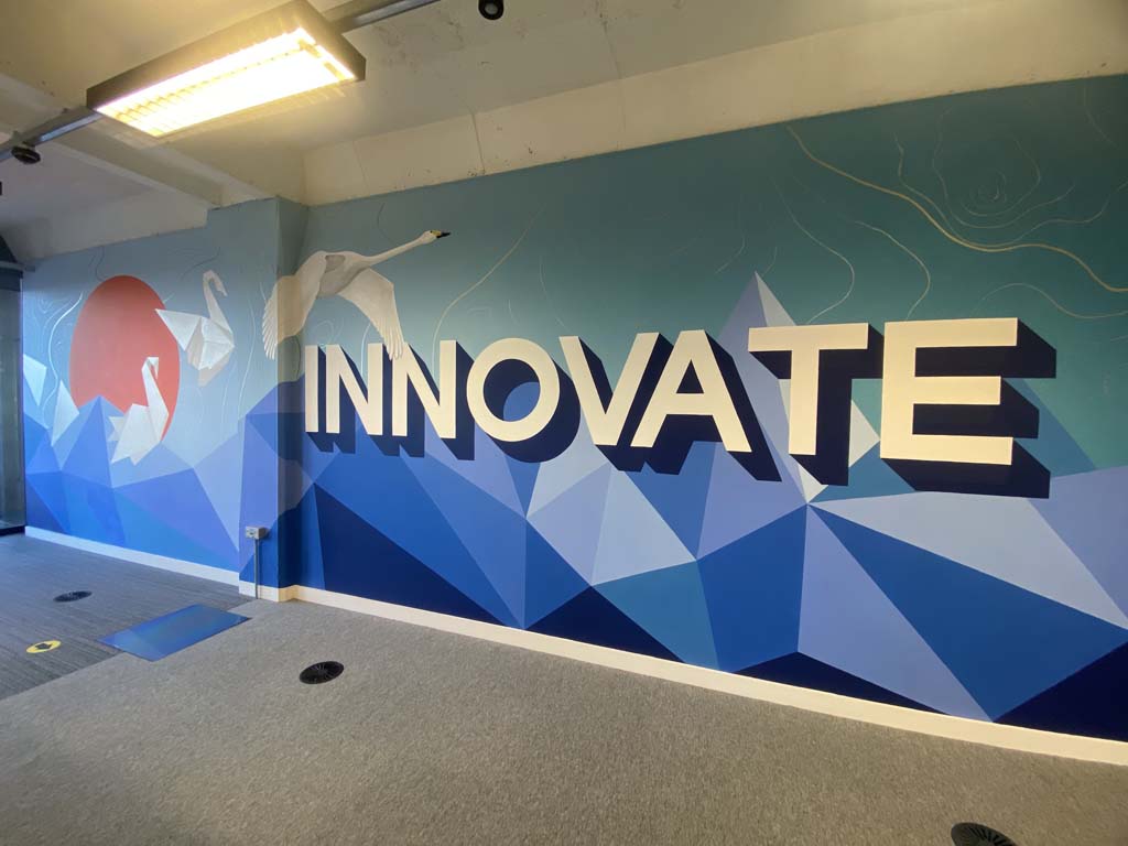 A vibrant abstract blue mural painted in an office. Featuring geometric patterns and a white swan flying over the word Innovate