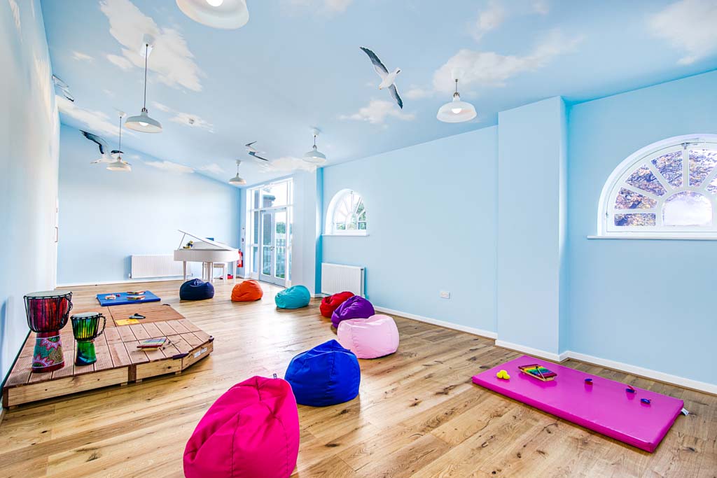 A room with walls painted like the sky, with a piano in the corner and bean bags on the floor